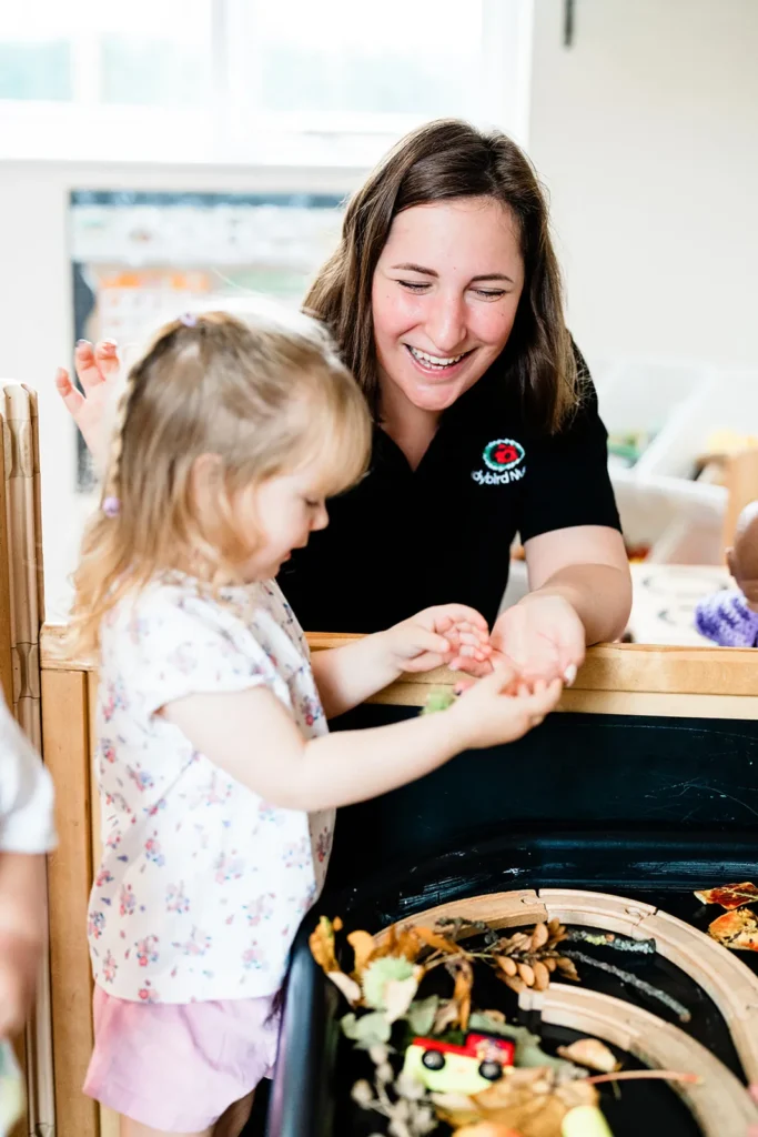 Practitioner smiling as a little girl explores the autumn leaves tray