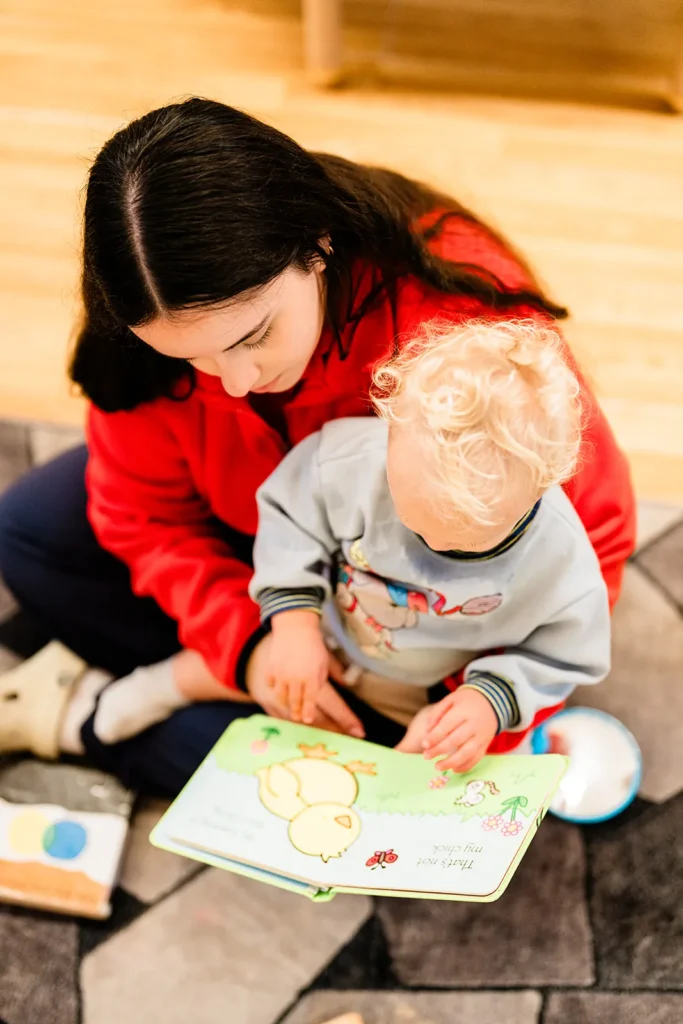 Practitioner in red reading a picture book with a toddler on her lap
